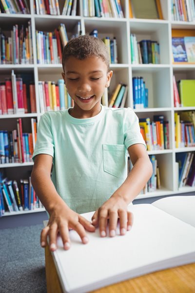 Young boy smiling while reading braille on table in library
