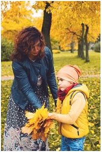 image of a woman and a child in a park where the child is holding a handful of leaves that the woman is also touching.