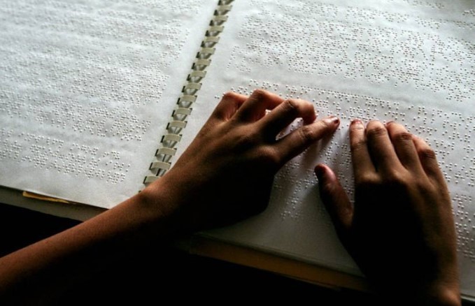 Picture of a braille book with hands going over the braille on the page.